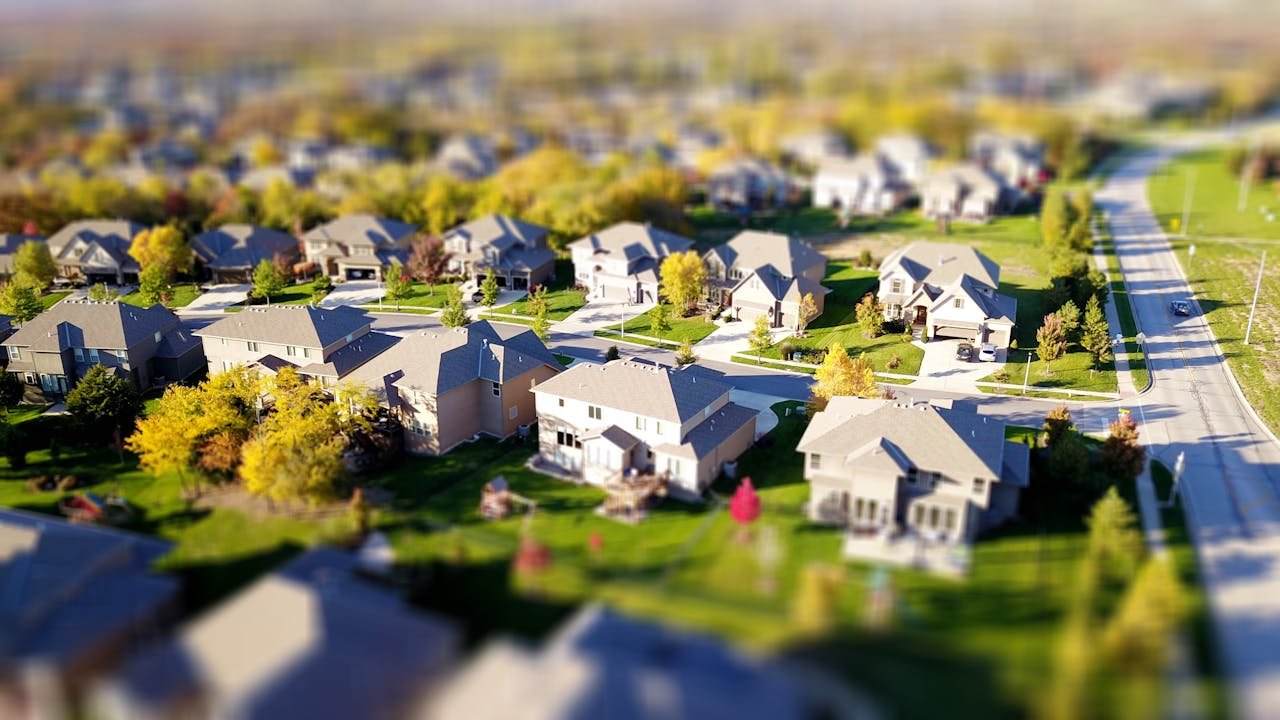 Home Tilt-shift aerial photo of a suburban neighborhood with green lawns and roads.
